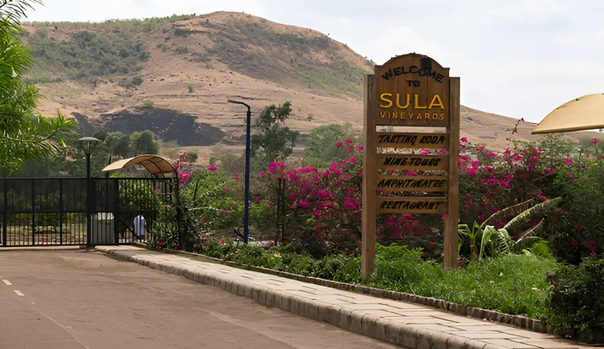 Entrance sign for Sula Vineyards surrounded by plants and flowers, with hills in the background.