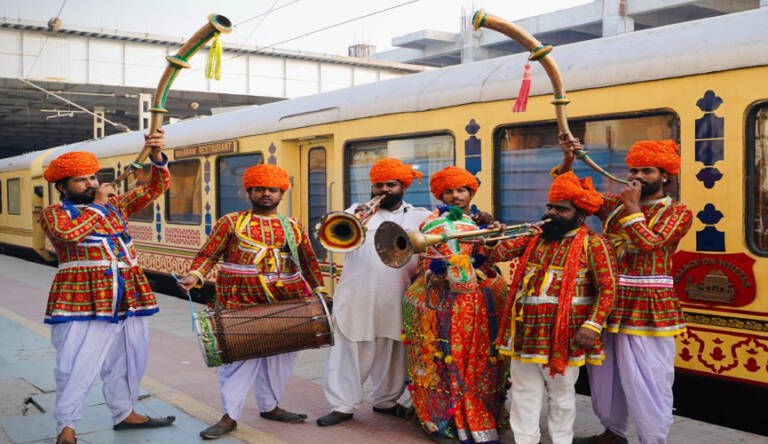 Musicians in traditional attire by a train.