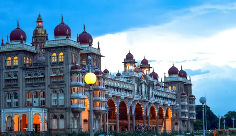 Mysore Palace illuminated at dusk against a cloudy sky.