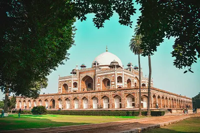 Humayun's Tomb in Delhi, India, viewed through a frame of green foliage.