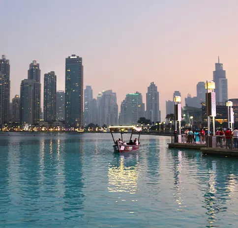 Dubai skyline reflecting in the water at dusk with a small boat in the foreground.