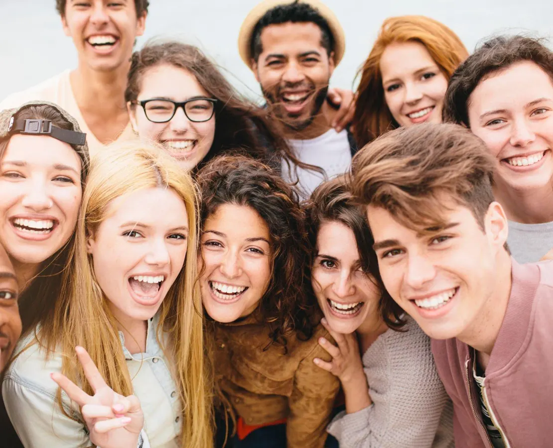 Large group of diverse young friends smiling and laughing in a close-up selfie.