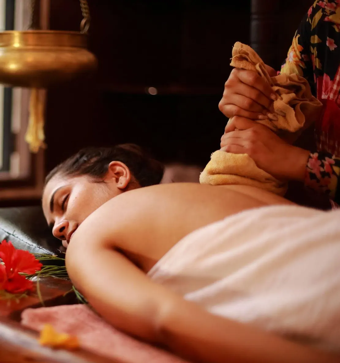 Woman receiving an Ayurvedic potli massage in a dimly lit spa.