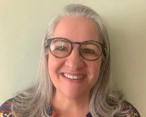 Smiling woman with gray hair wearing round tortoise-shell glasses.