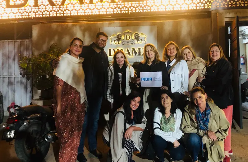 Group of tourists and a guide posing in front of a sign, holding a small 'INDIA Travel Factory' sign.