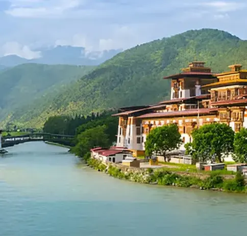 Punakha Dzong fortress next to a blue river, with lush green mountains in the background in Bhutan.