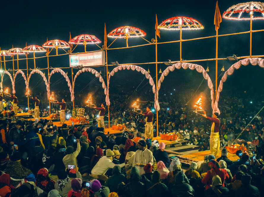 Varanasi evening aarti ceremony: Hindu priests perform ritual with flaming lamps under lit arches, large crowd gathers on Ganges river ghats