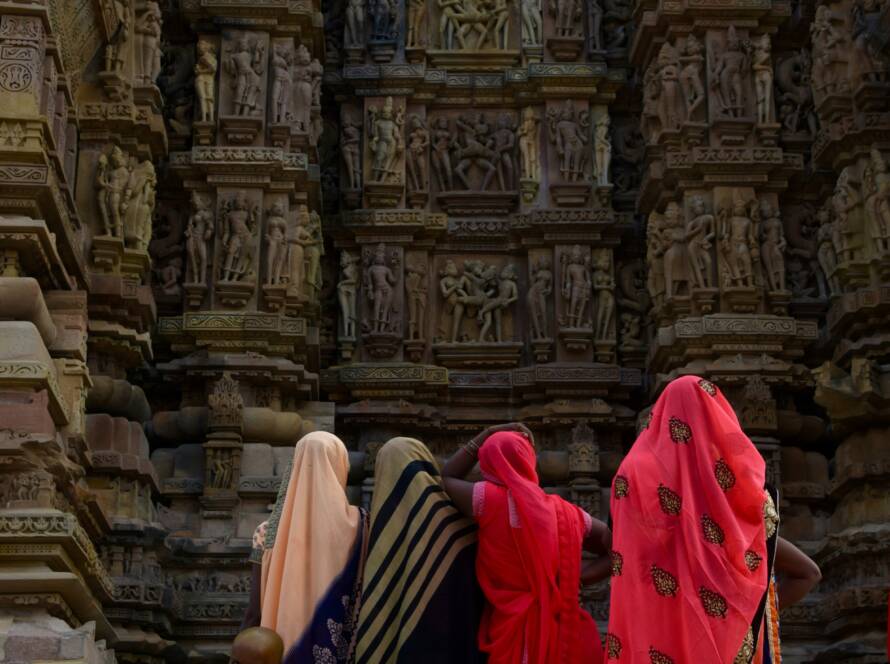 Women in vibrant sarees admiring intricate stone carvings at Khajuraho Temples, showcasing Iconic Monuments in India.