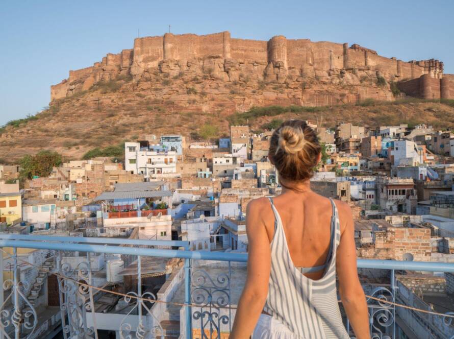Mehrangarh Fort Jodhpur: Massive sandstone fortress towering above Blue City with traveler viewing from terrace with blue railing