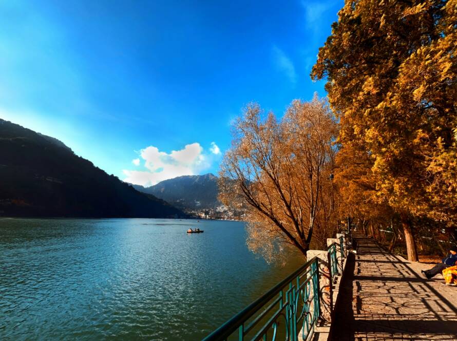 Calm lake with surrounding hills, trees, and a scenic walkway in Nainital, capturing the serenity of the Best Hill Stations in India.
