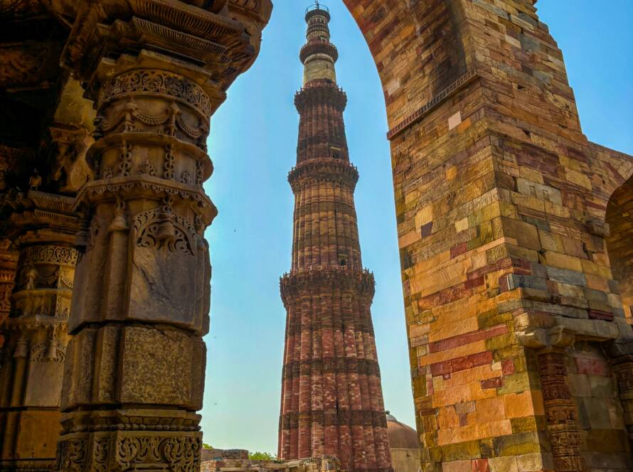 Intricately carved stone archway framing the towering Qutab Minar in Delhi, a striking example of Iconic Monuments in India.