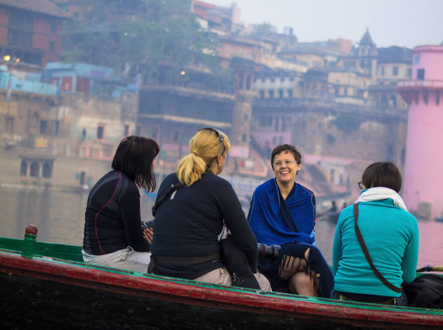 Travelers on boat ride along River Ganges in Varanasi with historic city, colorful buildings, and foggy riverbank in background