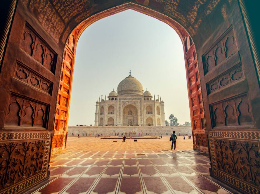 Taj Mahal Agra: White marble mausoleum with dome framed through ornate red sandstone archway with intricate inlay work