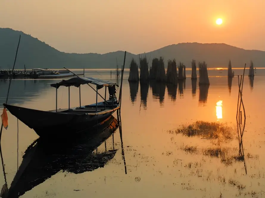 A boat docked in the still waters of Chilika Lake, Odisha, at sunset, with hills and fishing nets visible, showcasing Underrated Places in India.