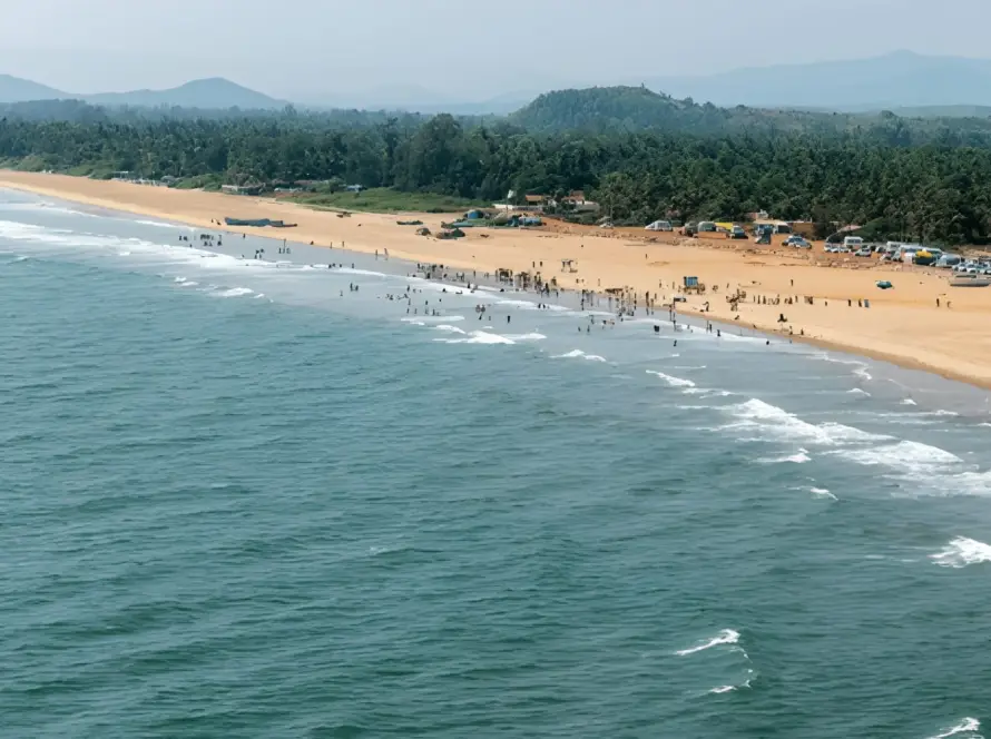 Aerial view of the long, sandy beach and blue ocean at Gokarna, Karnataka, backed by palm trees and hills, one of the Underrated Places in India.