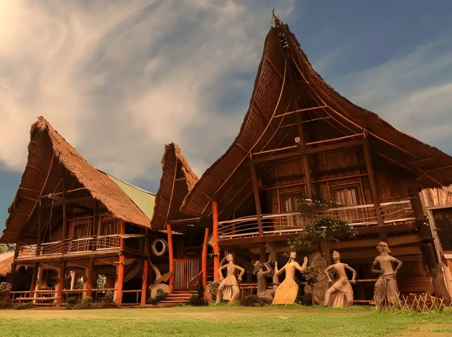 Traditional Mishing tribal stilt houses with large thatched roofs on Majuli Island, Assam, featuring cultural statues in front, one of the Underrated Places in India.