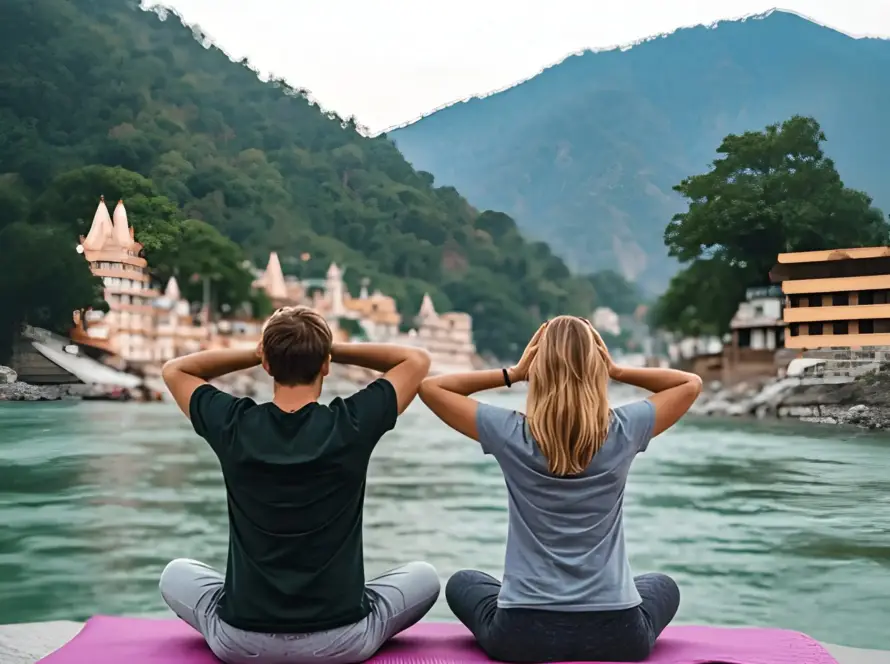 A couple meditating by the Ganges River in Rishikesh, with temples and mountains in the background, promoting Honeymoon Destinations in India.